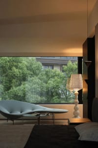 A modern bedroom featuring a glass window with a view of green trees outside.
