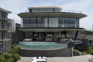 A modern house featuring a concrete exterior and glass elements with a person relaxing in the pool.