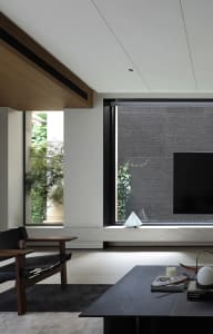 Modern living room with wooden armchair, coffee table, and concrete floor, featuring a television and plants.