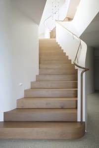 A modern wooden staircase with white walls and a curved handrail.