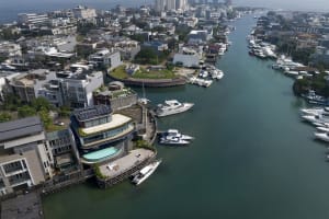 Aerial view of a waterfront development featuring concrete, glass, and timber structures with a pool and marina.