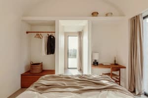 A minimalist bedroom with a wooden bed and wardrobe, featuring a simple design and natural materials, with a door leading to 