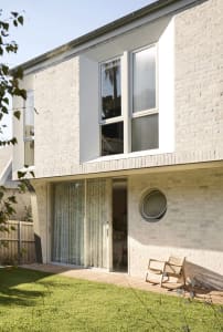 A modern residential exterior with white brick walls and large windows.