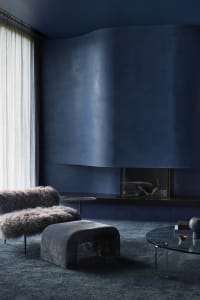 A modern industrial living room features plush, fur-covered seating and a sleek, glass-top coffee table with minimalist decor