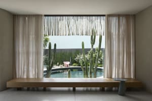 Minimalist residential interior with a large window overlooking a pool and cactus garden.