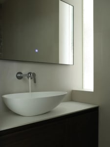 Modern minimalist bathroom with white ceramic sink and faucet, tall mirror, and frosted glass window.
