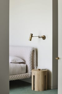 A minimalist bedroom featuring a bed with a quilted headboard, a bedside table made of light-colored wood, and a wall-mounted