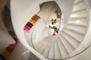 A white marble spiral staircase with glass railings and a potted plant.