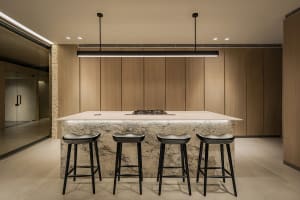 A modern kitchen with wooden cabinets, marble countertops, and black stools.