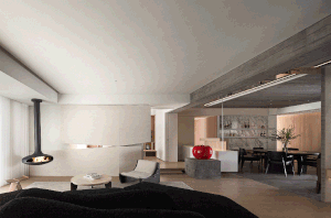 Modern living room with concrete fireplace, minimalist furniture, and red decorative apple on concrete pedestal.
