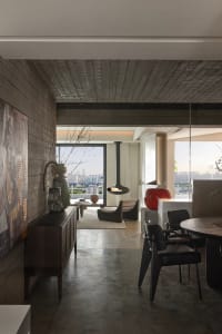 A modern living room with concrete walls and wooden flooring, featuring a hanging fireplace and large windows overlooking a c