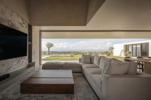 Modern living room with concrete walls and a view of the outdoor landscape, featuring a large sectional sofa and a low coffee