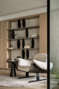 A minimalist living area featuring a white leather armchair, a small round side table with a glass drink container, and a bui