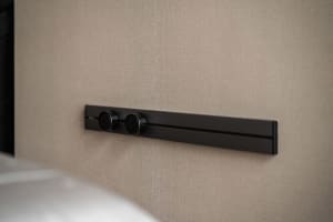 Modern interior lighting fixture with dark aluminum finish mounted on a beige fabric wall.