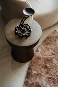 A modern side table with a black metallic chain decorative piece on top, sitting next to a beige leather sofa on a brown text