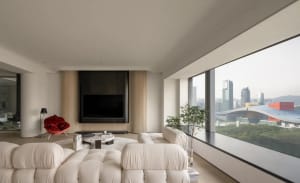 Modern living room with a neutral color palette, featuring a comfortable seating area, a flat-screen TV, and large windows wi