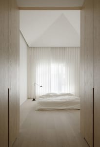 A minimalist bedroom with a bed, lamp, and sheer curtains.