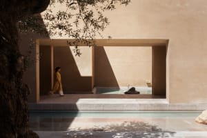 A minimalist architectural landscape featuring sandstone walls and an open space with a pool and sculpture.