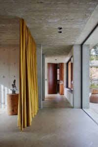 Modern minimalist interior with concrete walls, floor, and ceiling, featuring yellow curtains and a wooden sculpture on a tre