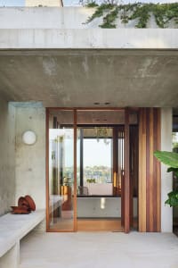 A modern entrance with a glass door and wooden accents, set against a concrete wall on a sunny day.