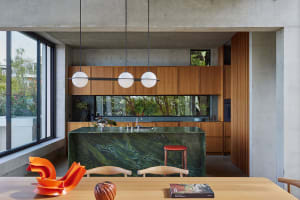 Modern residential kitchen featuring a marble island counter, wooden cabinets, and concrete walls.