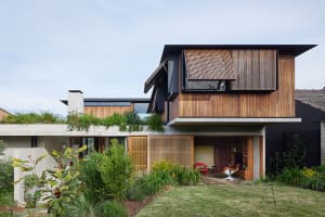 A modern house featuring a combination of concrete and wood exteriors, with a greenery rooftop and a partially open wooden ga