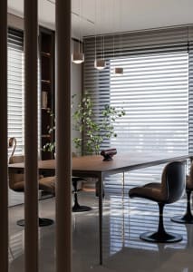 A modern dining room featuring a wooden table with black chairs, minimalist decor, and large windows with blinds.