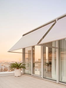 Modern balcony featuring white concrete flooring, fabric sunshade, and glass walls.