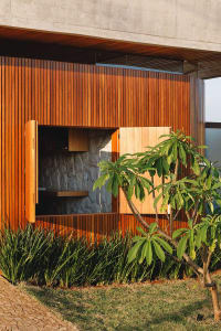 Modern house exterior featuring wooden panels and a stone wall for outdoor kitchen.