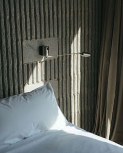 A minimalist bedroom with a concrete textured wall and a white pillow on a bed.