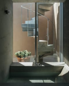 Concrete spiral staircase with metal railing inside a building with large windows.