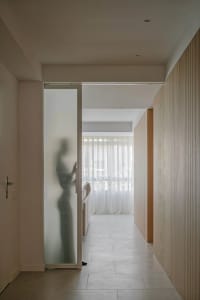 A modern minimalist interior with white marble flooring, frosted glass sliding door, and light-colored wooden walls.