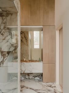 A sleek, contemporary bathroom with marble tiles, a glass shower enclosure, and wooden cabinetry.