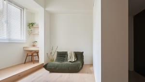 A modern minimalist living room with a green plush sofa, a wooden stool under a white window with blinds.