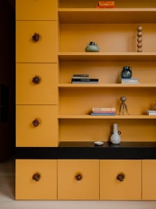 A modern storage shelf with yellow painted cabinets and drawers, featuring decorative objects and books.