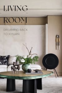 A modern living room featuring metallic furniture and a round glass-top coffee table with a vase of white orchids and greener