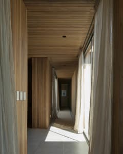 A modern minimalist corridor featuring wooden walls and floor-to-ceiling windows with sheer curtains.