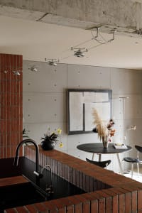 A minimalist kitchen with brick countertops and a concrete wall featuring modern track lighting and an abstract artwork.