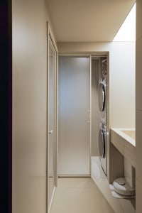 A minimalist modern bathroom and laundry room with tiled walls, featuring a clear shower door and washing machines.