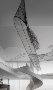 A modern metal sculpture hangs from the ceiling in an interior design setting.