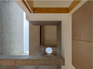 Modern interior with concrete walls and wooden accents, featuring a circular skylight and natural light.