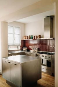 A modern kitchen with a metal island, stainless steel appliances, and a red-tile backsplash displaying a variety of ceramic v