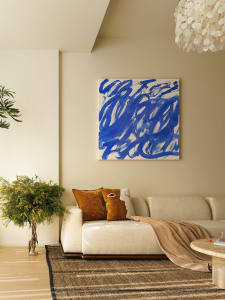 A minimalist living room featuring a white sofa with blue and white abstract art above, a wooden coffee table, and a woven ru
