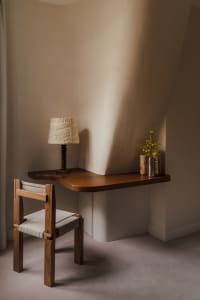 A modern home office setup featuring a wooden desk and chair, with a lamp and flowers on the desk.