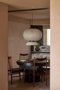 Modern minimalist dining room featuring a round wooden table with marble top, wooden chairs, and pendant lighting over the ta