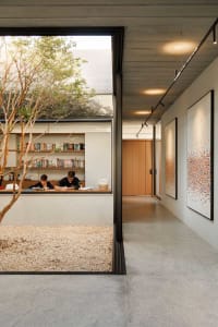 A modern home office space with concrete and glass elements, featuring two individuals working at a desk.