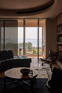 Modern living room with a leather sofa, round wooden table, and floor-to-ceiling view of the lake.