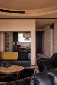 Modern living room featuring a black leather sofa, wooden coffee table, and stone fireplace.