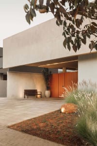 Concrete driveway with bench, potted plant, and garden in front of a modern house.