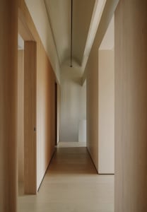 A minimalist corridor with wooden walls and floors, arch-shaped ceiling details, and arch-shaped openings for doors.